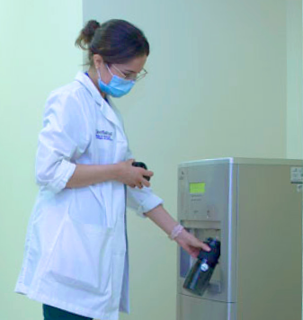 Mujer joven con uniforme de hospital rellenando un termo en purificador modelo D8